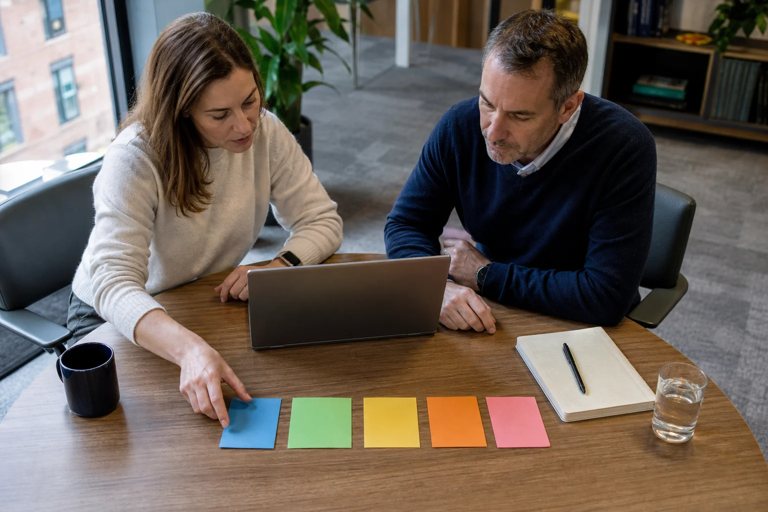 Illustrative photograph of two UK consultancy managers reviewing an enquiry beside five coloured workflow cards