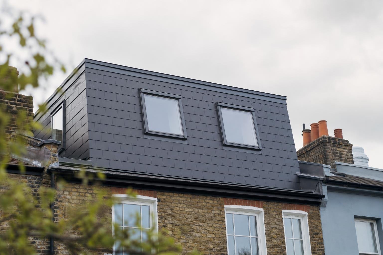 A completed dormer loft conversion on a London terrace house with new skylights under a bright overcast sky